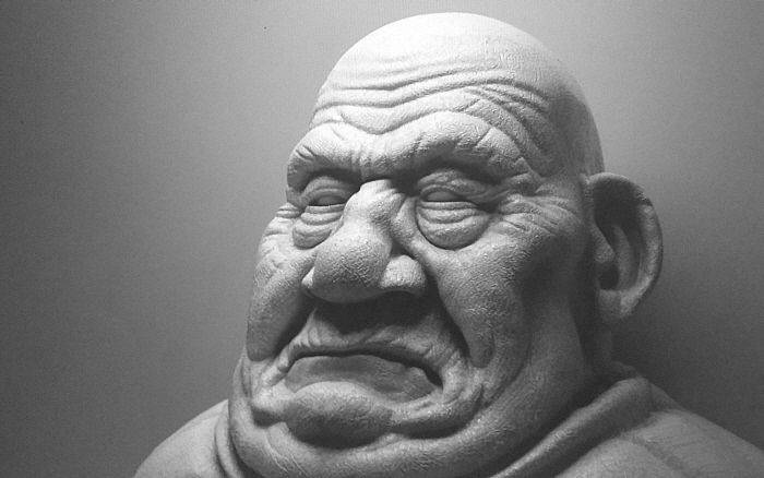 A grey sculpted bust of an old man's wrinkled, scowling face